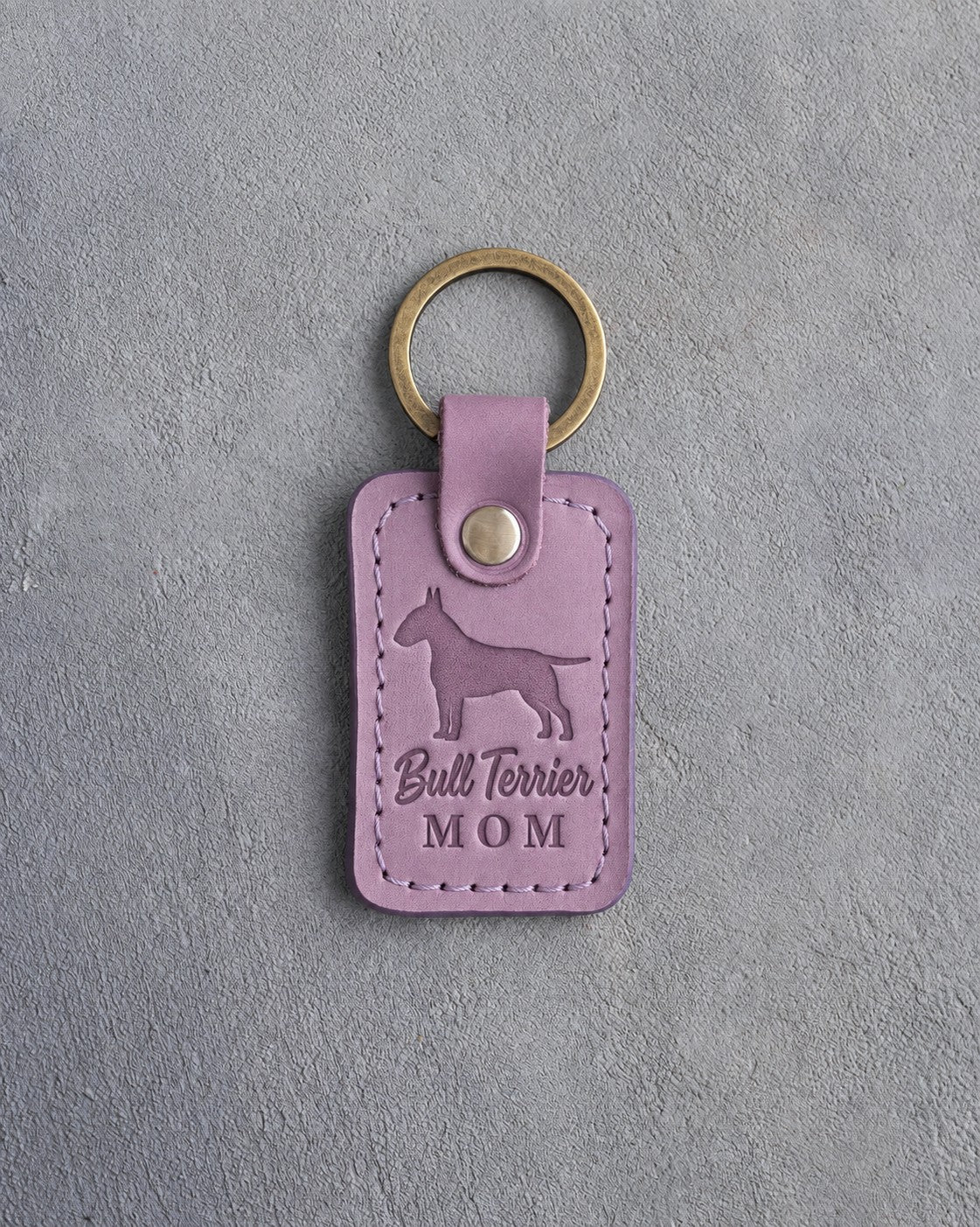 Lilac leather keychain with a debossed Bull Terrier and the words Bull Terrier MOM, on gray concrete