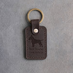 Dark espresso leather keychain debossed with an egg-headed Bull Terrier above Bull Terrier and THE BULLY, on gray concrete
