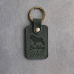 Forest green leather keychain debossed with a bulldog silhouette and Bulldog DAD on gray concrete