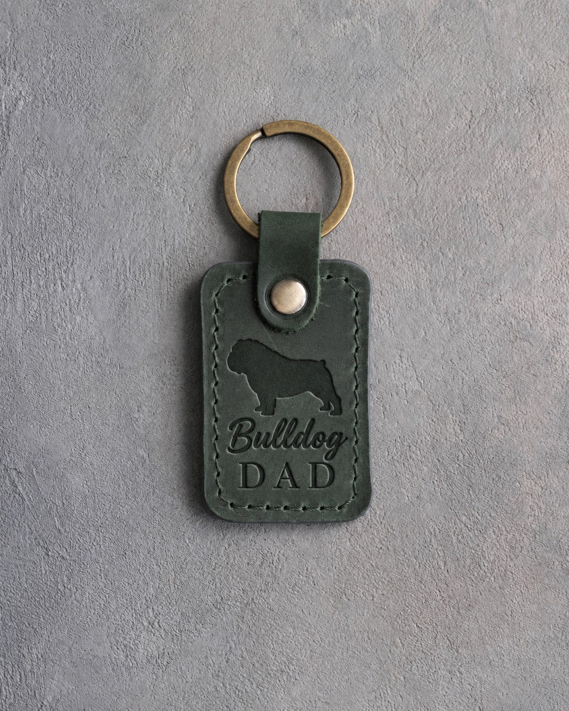 Forest green leather keychain debossed with a bulldog silhouette and Bulldog DAD on gray concrete