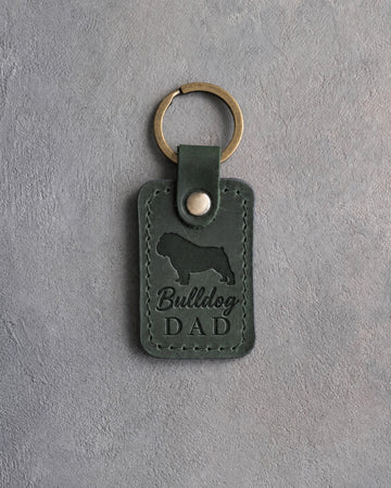 Forest green leather keychain debossed with a bulldog silhouette and Bulldog DAD on gray concrete