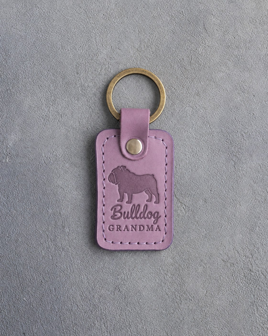 Lilac leather keychain debossed with an English bulldog silhouette and the words Bulldog GRANDMA, on gray concrete