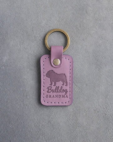 Lilac leather keychain debossed with an English bulldog silhouette and the words Bulldog GRANDMA, on gray concrete