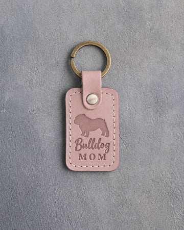 Blush pink leather keychain with a debossed English bulldog and the words Bulldog MOM, on gray concrete