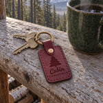 Cabin Christmas keychain in wine red leather on an iron key hanging from a cabin door latch with snow on the step