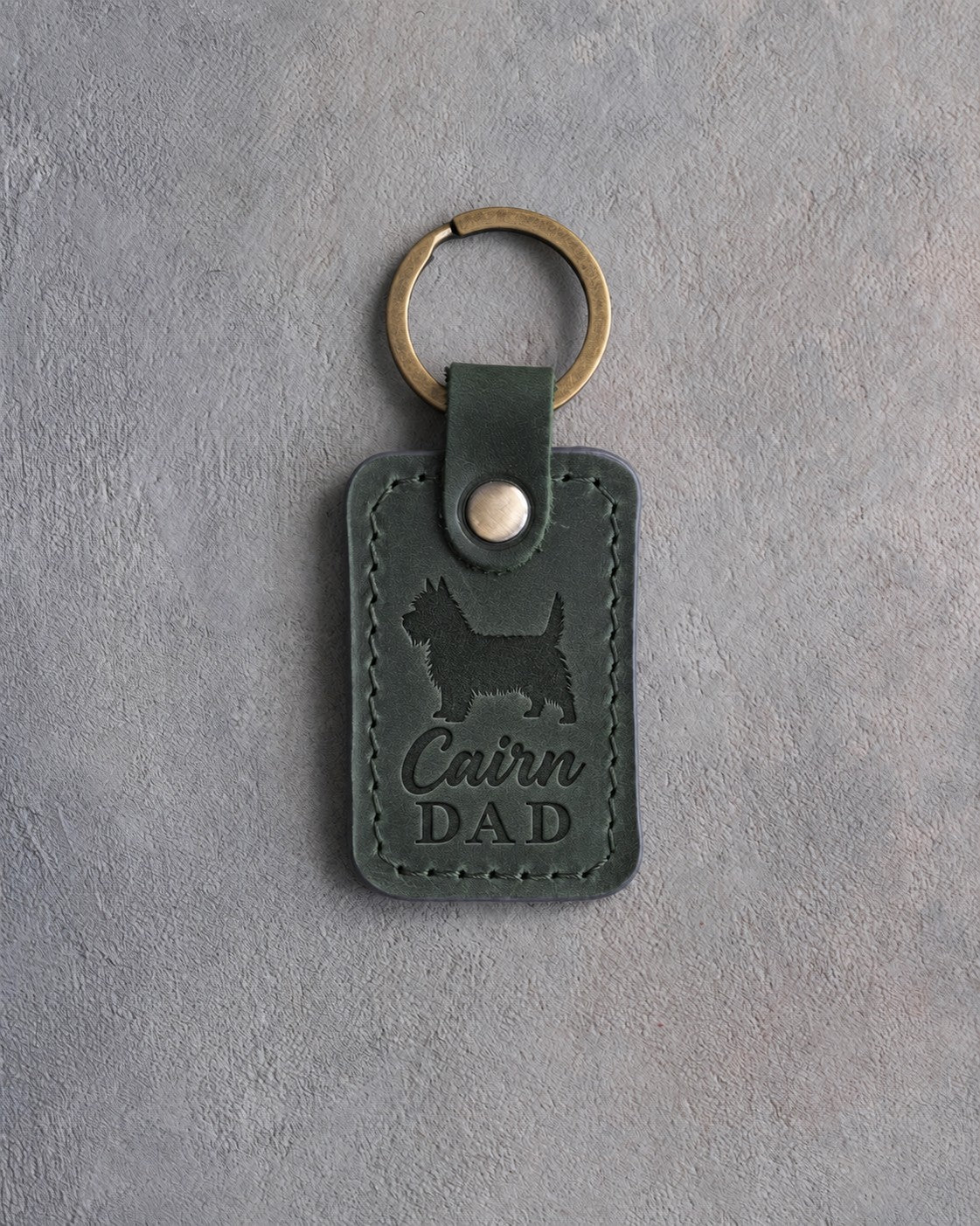 Forest green leather keychain debossed with a Cairn Terrier silhouette and the words Cairn DAD, on gray concrete
