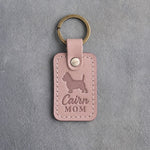 Blush pink leather keychain debossed with a Cairn Terrier silhouette and the words Cairn MOM, on gray concrete
