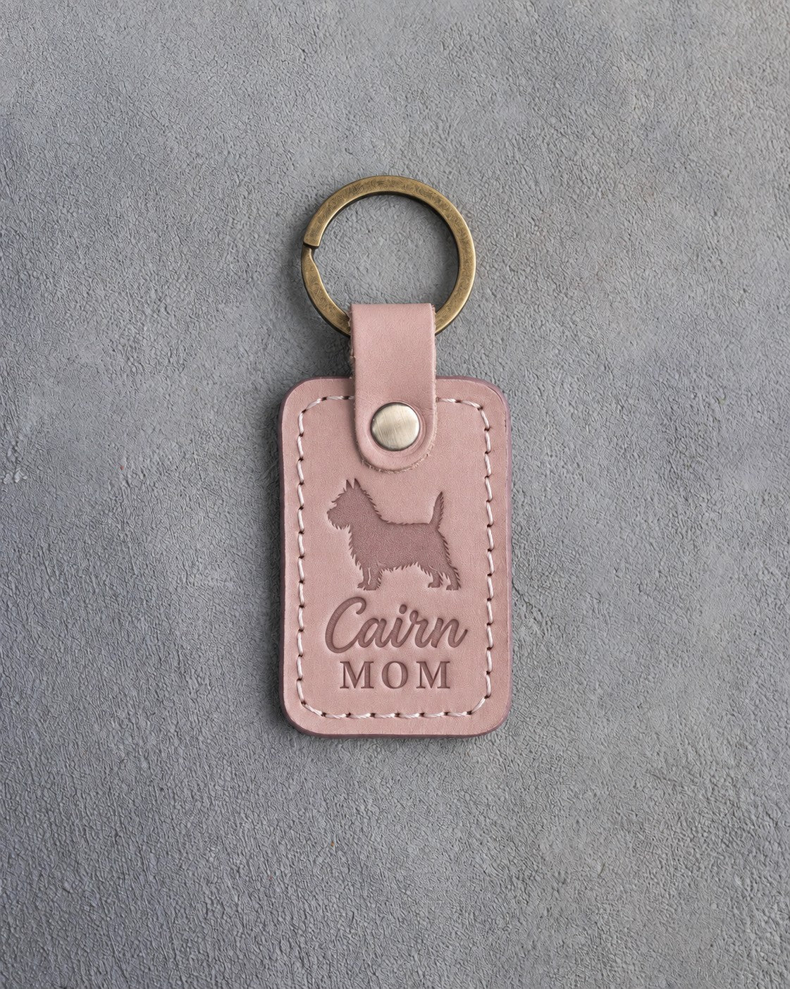 Blush pink leather keychain debossed with a Cairn Terrier silhouette and the words Cairn MOM, on gray concrete