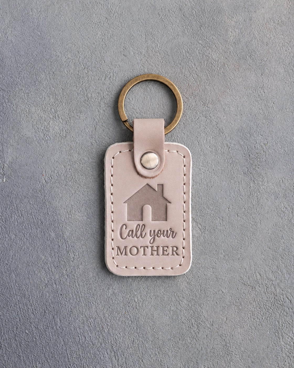 Gray sand leather keychain debossed with a gabled house above Call your and MOTHER