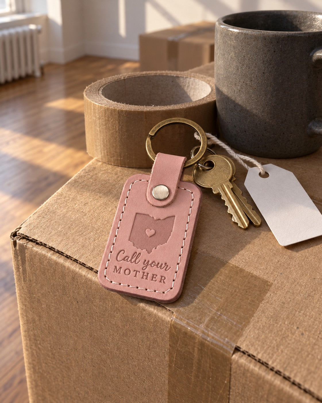 Pink Call Your Mother keychain on a dorm room key beside a stack of textbooks on a desk