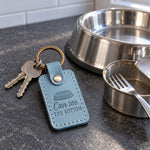 Turquoise Can See the Bottom keychain on a kitchen floor next to a cat food bowl