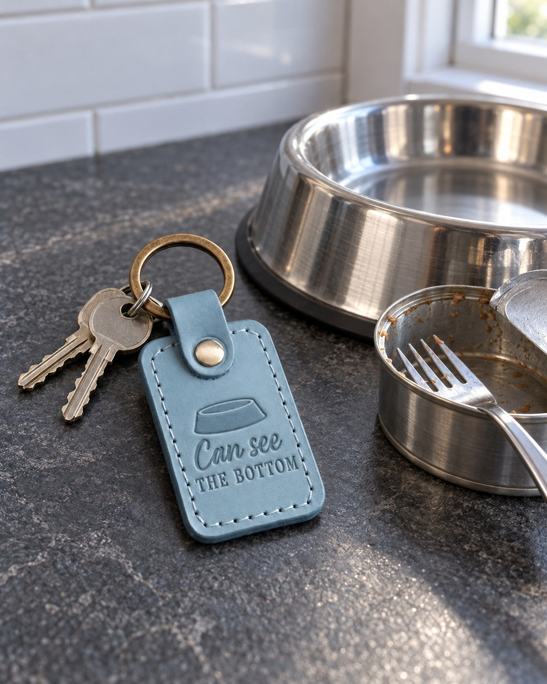 Turquoise Can See the Bottom keychain on a kitchen floor next to a cat food bowl