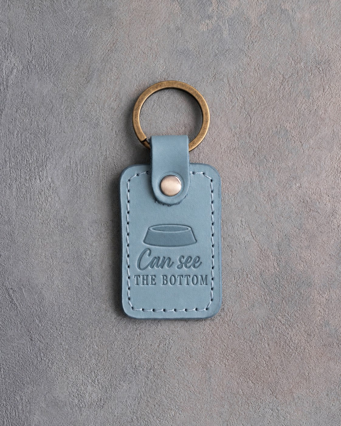 Turquoise leather keychain debossed with an empty cat food bowl above the words Can see THE BOTTOM