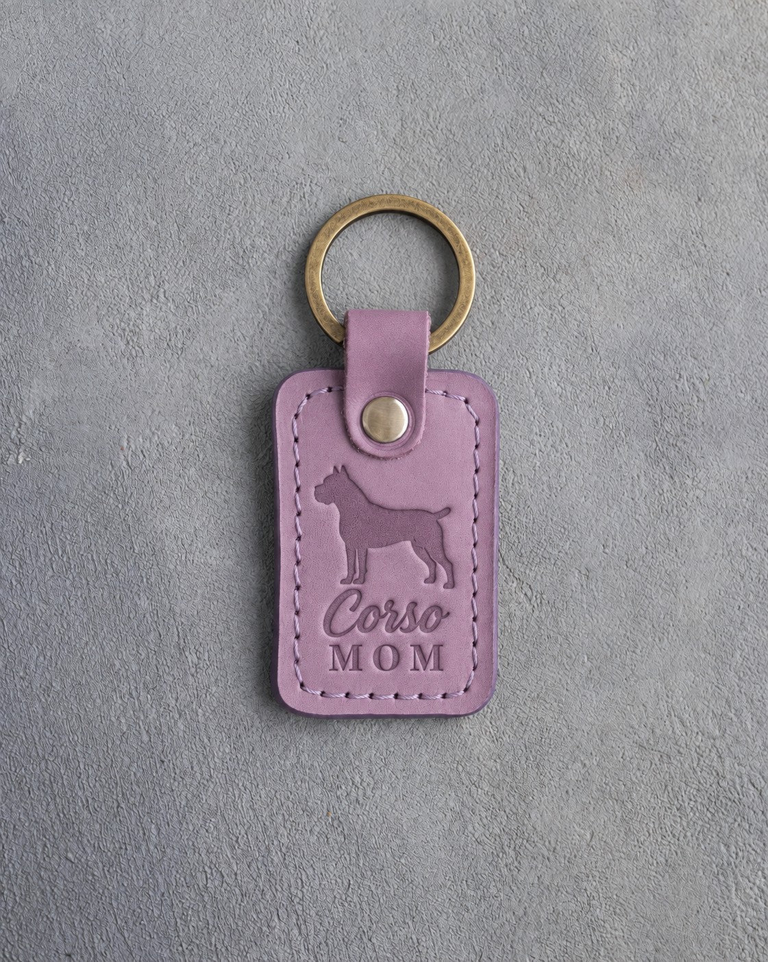 Lilac leather keychain with a debossed Cane Corso and the words Corso MOM on gray concrete