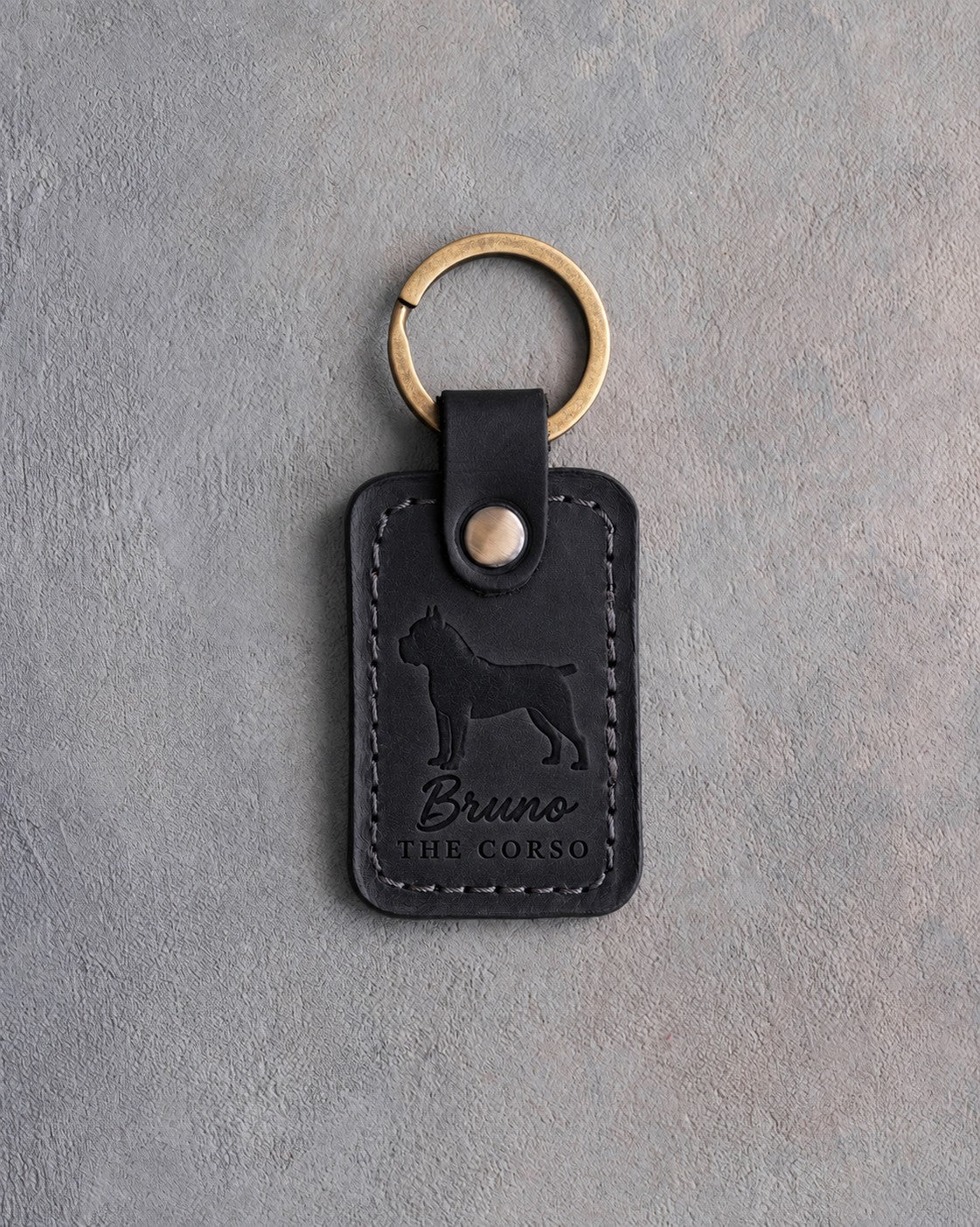 Black leather keychain debossed with a Cane Corso above the name Bruno and THE CORSO, on gray concrete