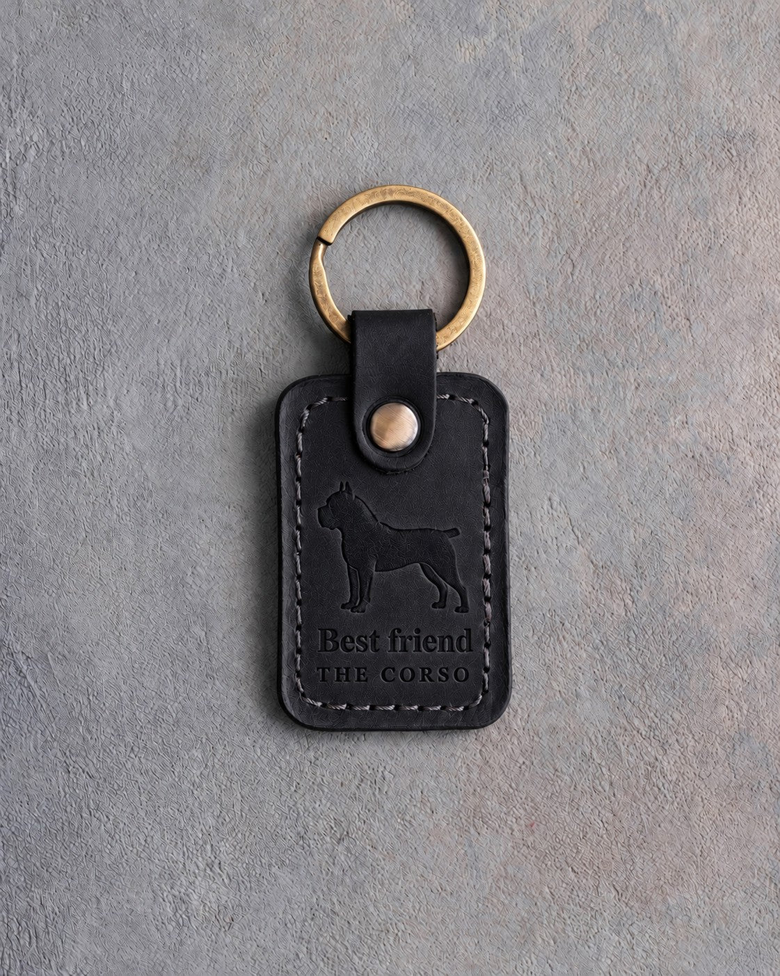 Black leather keychain debossed with a Cane Corso above Best friend and THE CORSO, on gray concrete