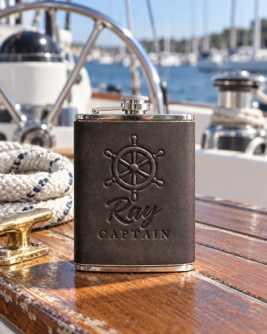 Dark espresso Ray CAPTAIN hip flask in full-grain leather on the worn teak cockpit table of a sailboat beside a coiled white dock line