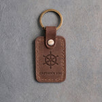 Sicilian Brown leather keychain debossed with a six-spoke ship's wheel above CAPTAIN'S LOG, on gray concrete