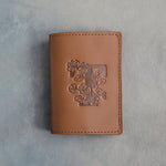 Caramel leather passport cover with a large floral initial F pressed into the front