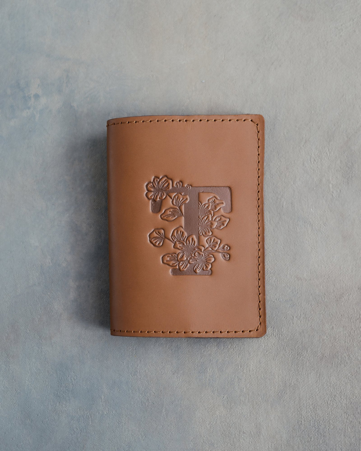 Caramel leather passport cover with a large floral initial F pressed into the front