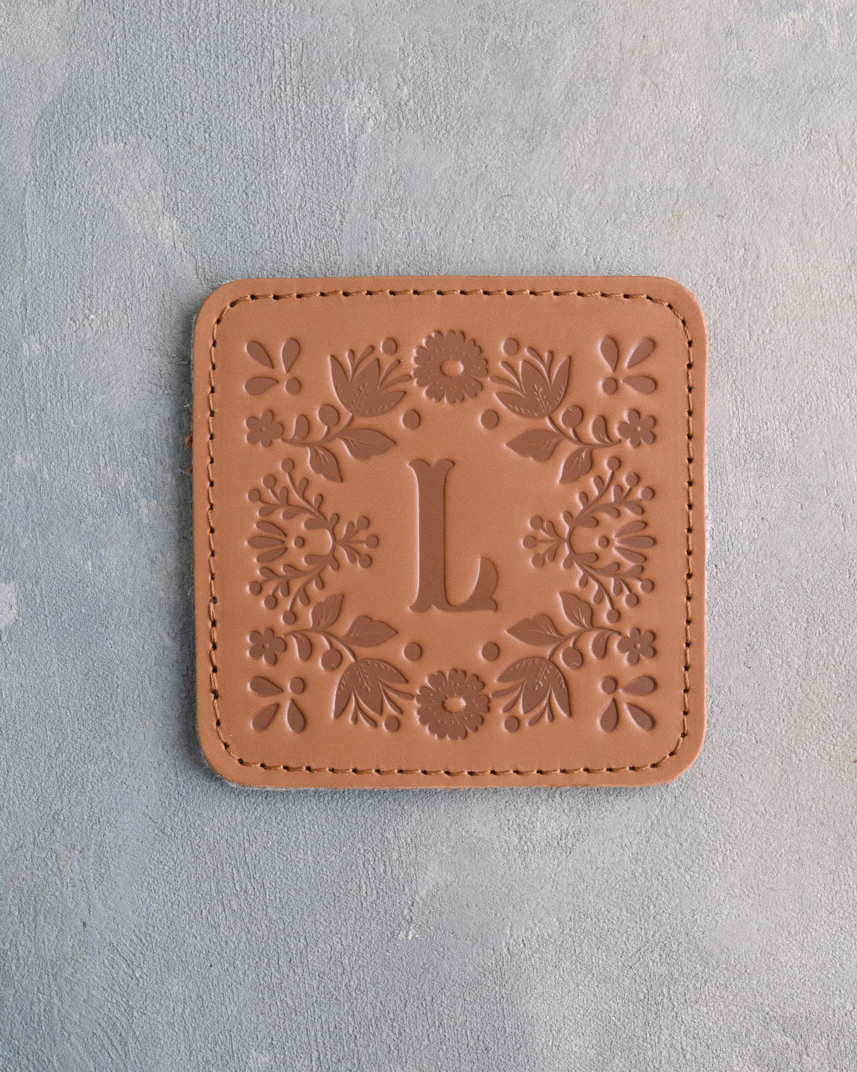 Caramel leather coaster with the floral frame and an initial pressed in