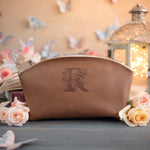 Caramel initial makeup pouch with a floral monogram, staged among pale roses on a slate table
