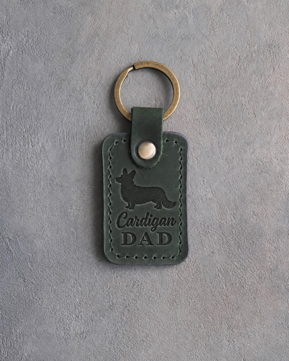 Forest green leather keychain debossed with a Cardigan Welsh Corgi silhouette and the words Cardigan DAD, on gray concrete