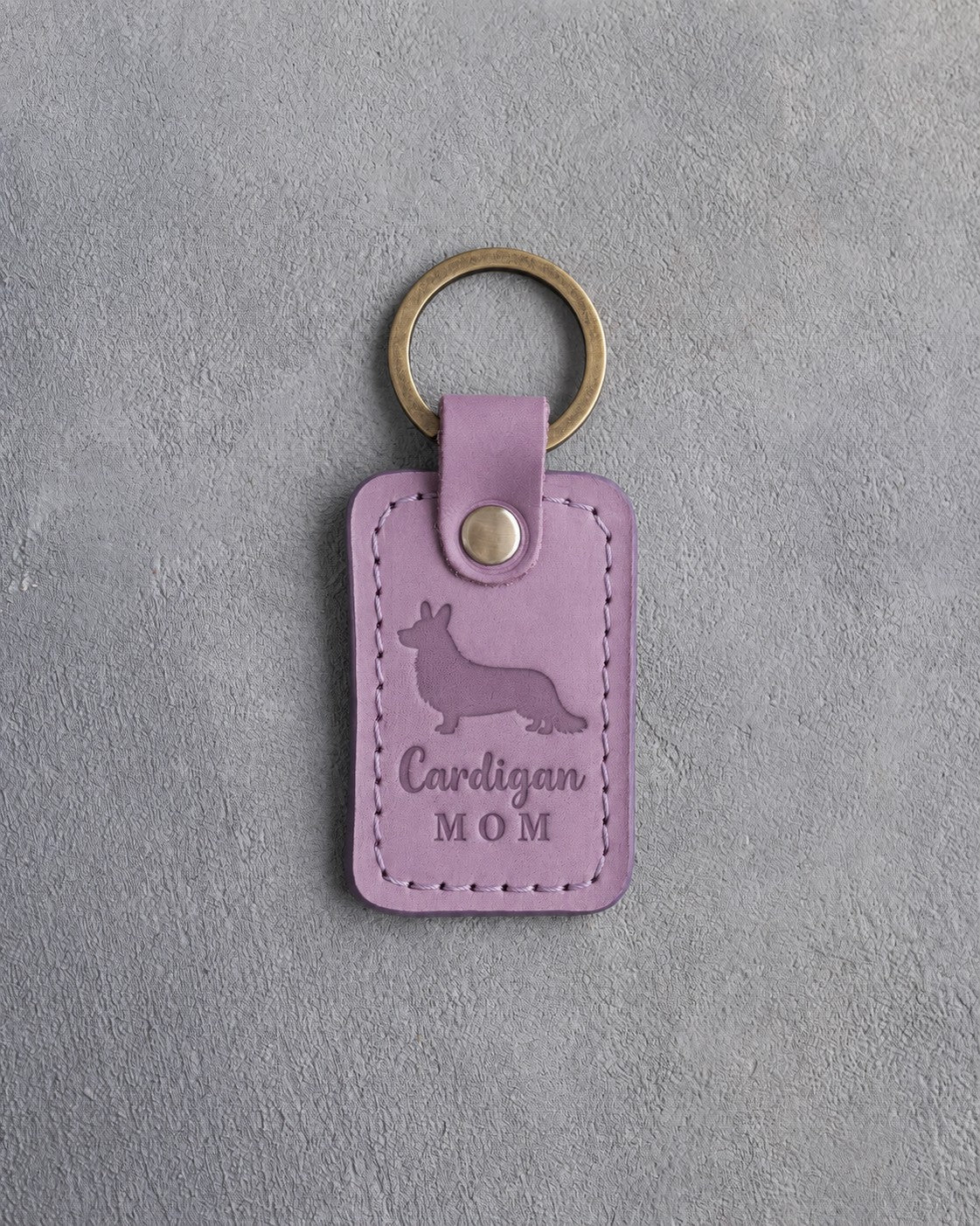 Lilac leather keychain debossed with a Cardigan Welsh Corgi silhouette and the words Cardigan MOM, on gray concrete