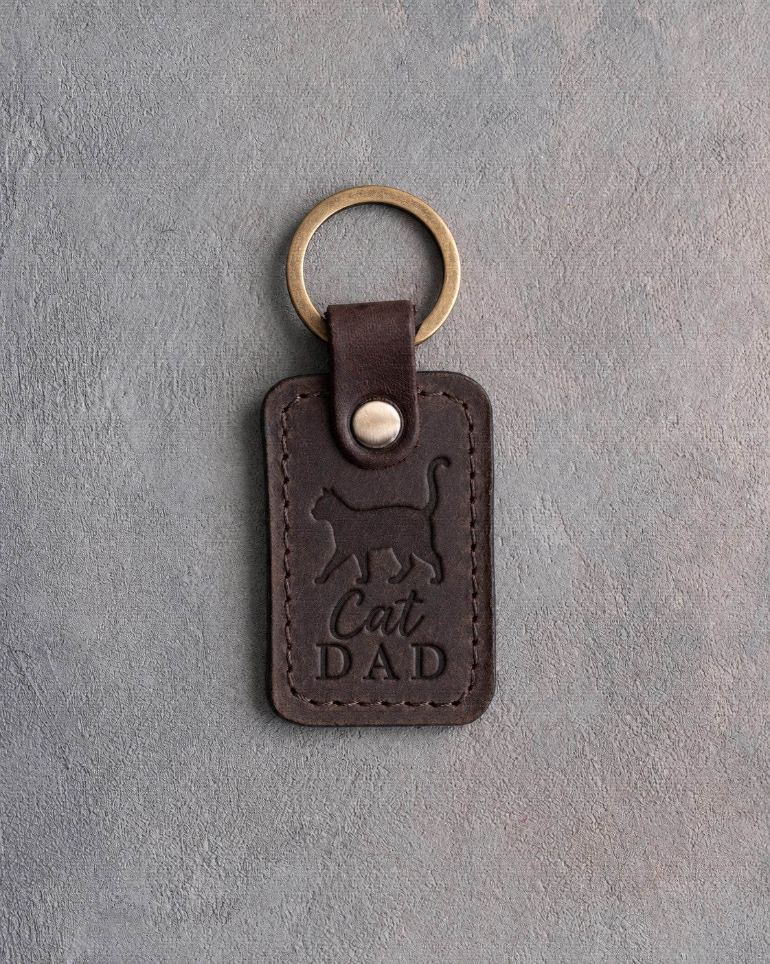 Dark espresso leather keychain debossed with a walking cat, tail straight up, above the words Cat DAD