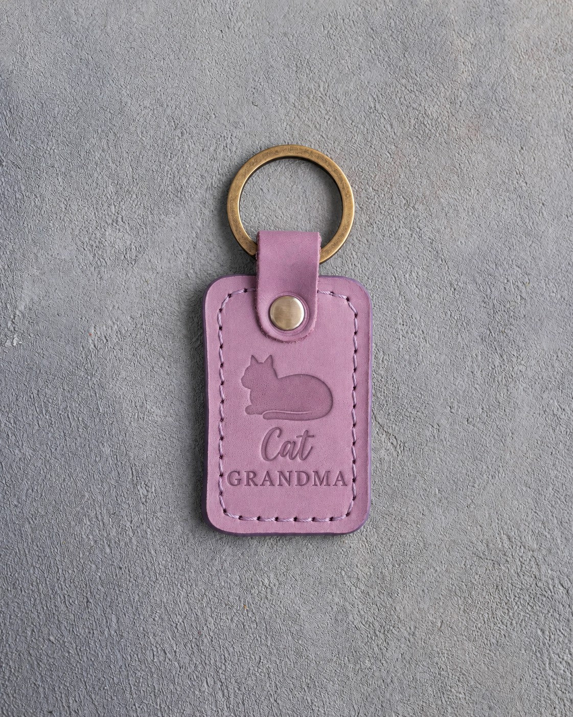 Lilac leather keychain debossed with a loafing cat, paws tucked under, above the words Cat GRANDMA