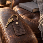 Dark brown Cat Grandpa keychain on the arm of a leather armchair in lamplight