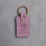 Lilac leather keychain debossed with a loafing cat, paws tucked under, above the words Cat LADY