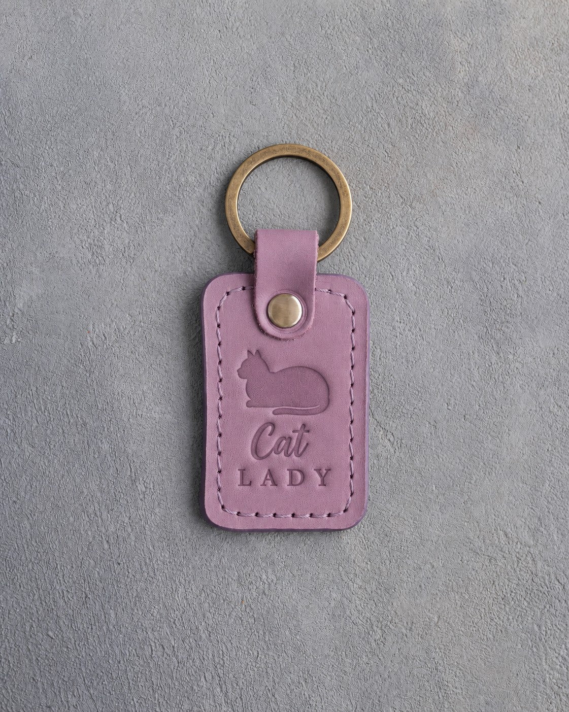 Lilac leather keychain debossed with a loafing cat, paws tucked under, above the words Cat LADY