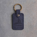 Blueberry navy leather keychain debossed with a cat on a windowsill above Forever and ON THE SILL, on gray concrete