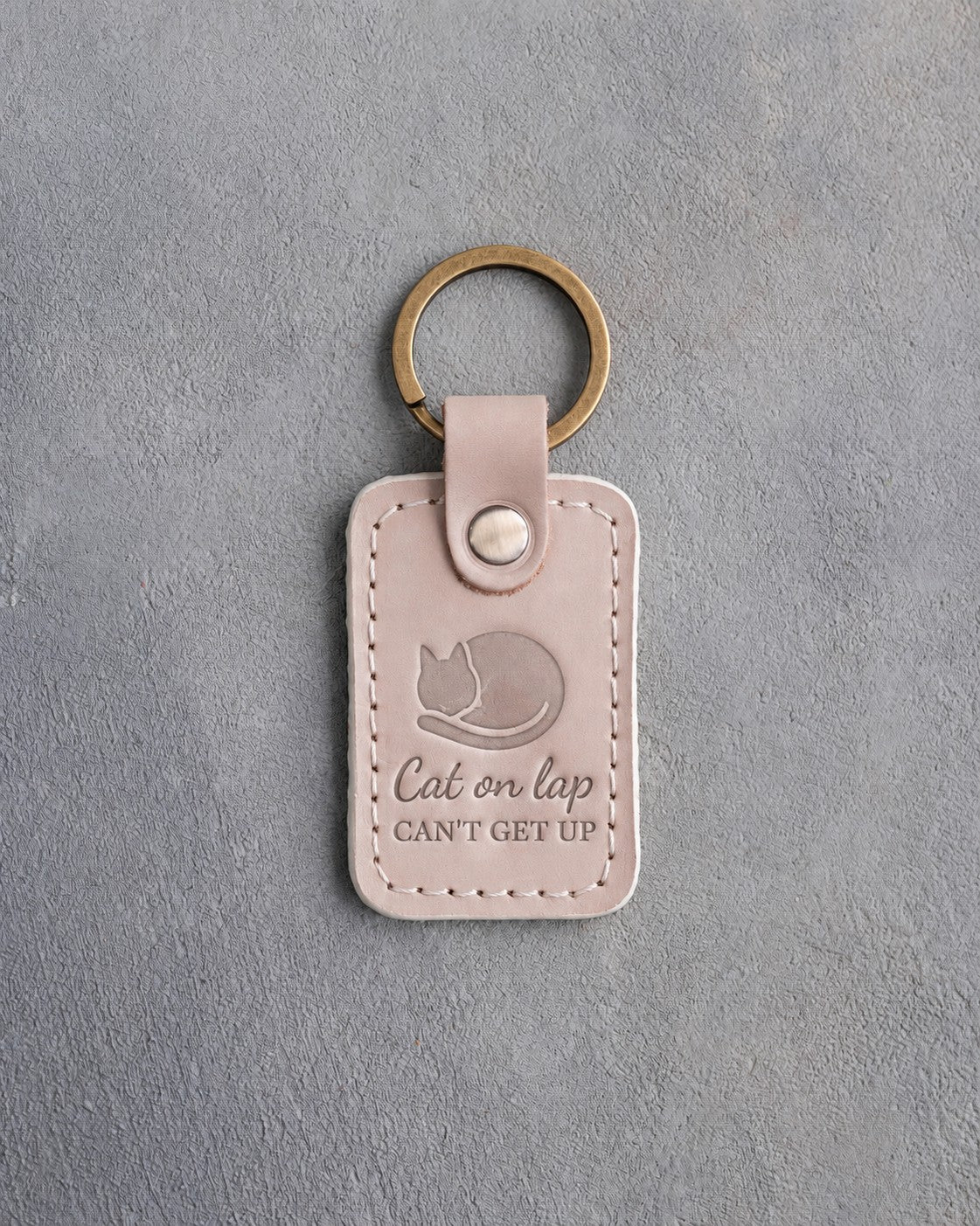 Gray sand leather keychain debossed with a curled sleeping cat above the words Cat on lap CAN'T GET UP