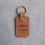 Caramel leather keychain debossed with a channel catfish above the words Catfish DAD, on gray plaster