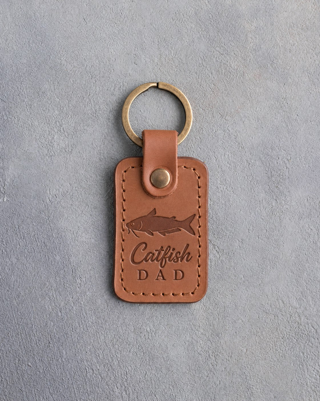 Caramel leather keychain debossed with a channel catfish above the words Catfish DAD, on gray plaster