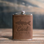 Sicilian brown leather-wrapped hip flask debossed with a channel catfish above Earl and CATFISH, on a wooden table