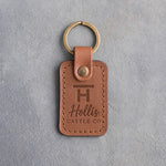 Caramel leather keychain debossed with a Bar H ranch brand above the name Hollis and CATTLE CO, on gray plaster