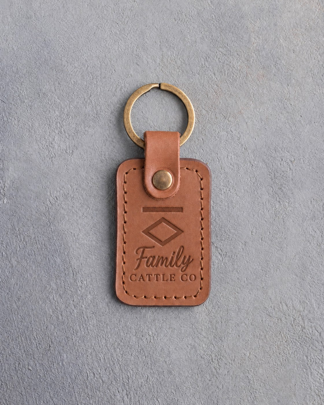 Caramel leather keychain debossed with a Bar Diamond ranch brand above Family and CATTLE CO, on gray concrete