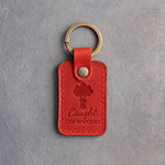 Poppy red leather keychain debossed with a hand-tied bouquet above the words Caught THE BOUQUET, on gray concrete
