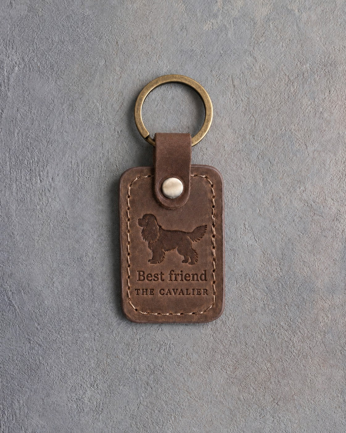 Sicilian brown leather keychain debossed with a Cavalier King Charles Spaniel silhouette above Best friend and THE CAVALIER, on gray concrete