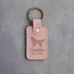 Blush pink leather keychain debossed with a Cavalier King Charles Spaniel silhouette and the words Cavalier MOM, on gray concrete