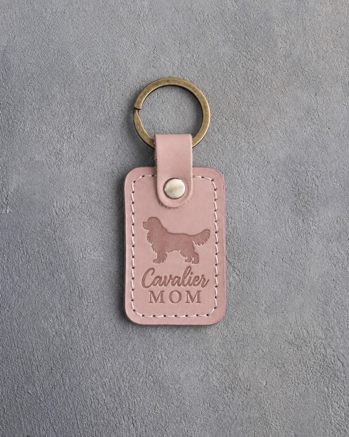 Blush pink leather keychain debossed with a Cavalier King Charles Spaniel silhouette and the words Cavalier MOM, on gray concrete