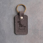 Country gray leather keychain debossed with a sitting puppy and a bone biscuit above Chewed THE LAST ONE, on gray concrete