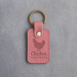 Parisian blossom pink leather keychain debossed with a hen above the words Chicken WHISPERER, on gray concrete