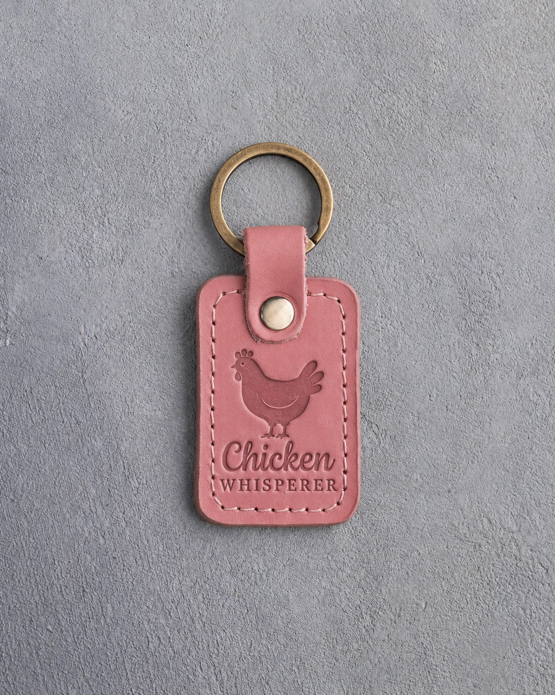 Parisian blossom pink leather keychain debossed with a hen above the words Chicken WHISPERER, on gray concrete