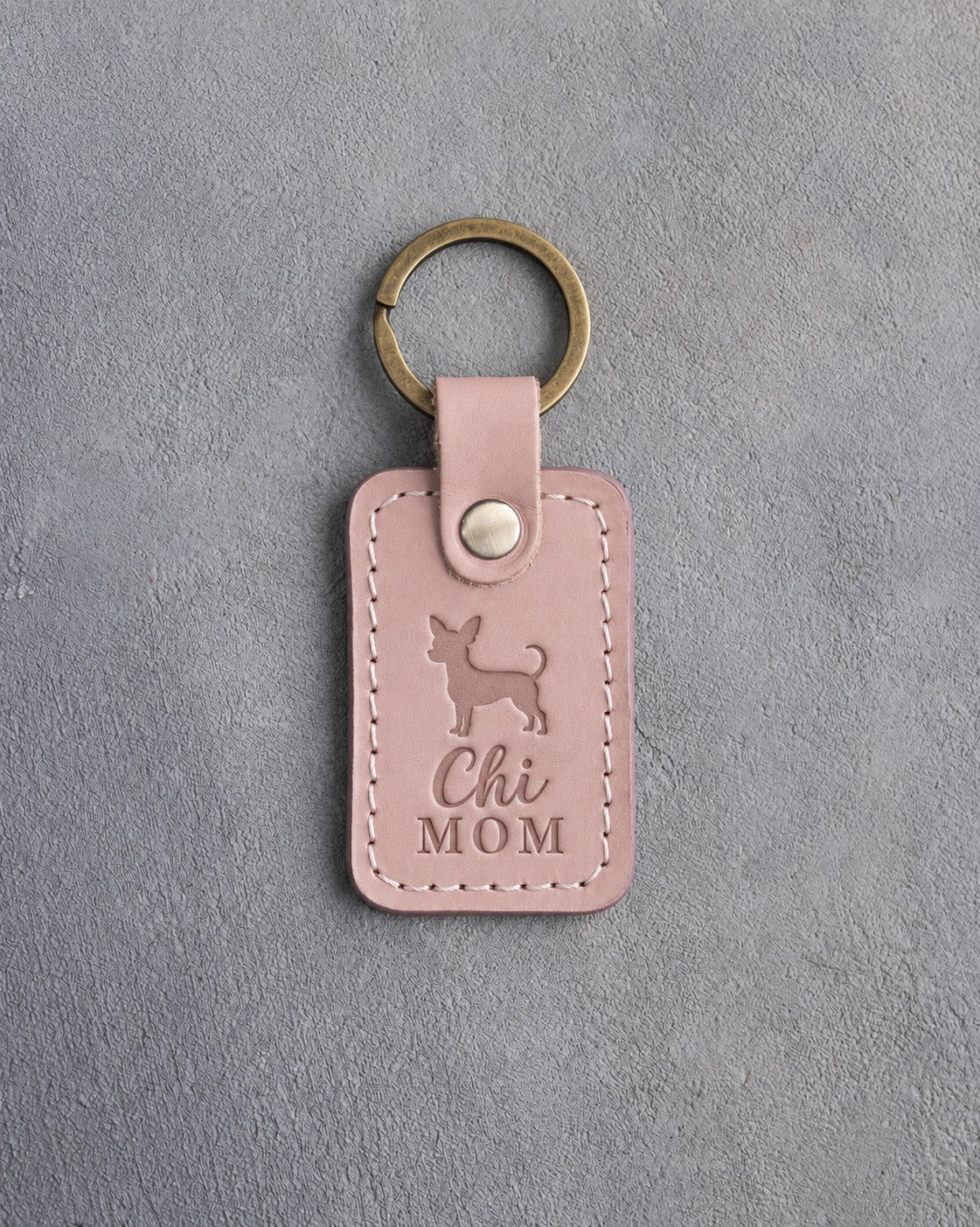 Blush pink leather keychain debossed with a chihuahua silhouette and the words Chi MOM, on gray concrete