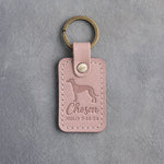 Blush pink leather keychain debossed with a greyhound above Chosen and MILO 3·14·24, on gray concrete