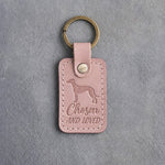 Blush pink leather keychain debossed with a greyhound above Chosen and AND LOVED, on gray concrete